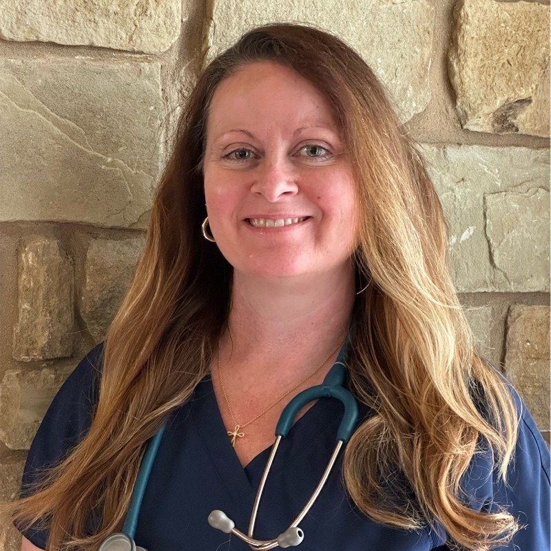 Kristina M. McGahan in navy scrubs with a teal stethoscope, photographed against a limestone wall.
